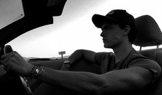 a man sitting in the driver's seat of a car with his hand on the steering wheel