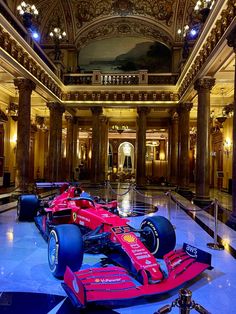 a red race car is on display in a museum with columns and chandeliers