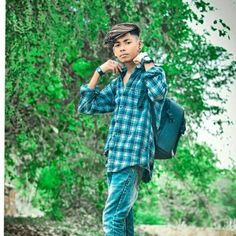 a young boy with a backpack is standing in front of a tree and looking at the camera