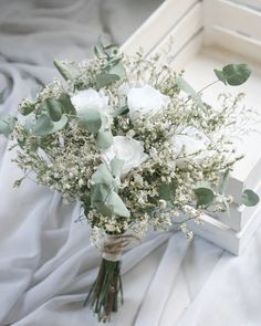 a bouquet of white flowers sitting on top of a table next to a box filled with greenery