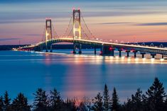 a bridge that is over water with lights on at the top and below it in the distance