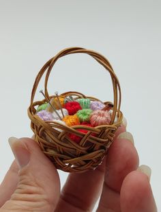 a hand holding a miniature basket with crochet balls in it and yarn on the inside