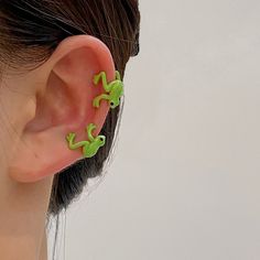 a close up of a person's ear with two small green geckos on it