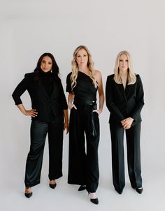 three women standing next to each other in black outfits