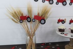 a table topped with cupcakes covered in frosting next to a vase filled with wheat