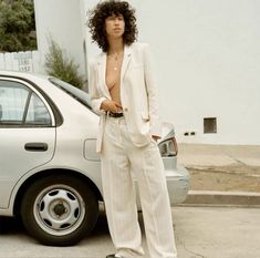 a woman standing next to a car in front of a white building wearing a suit