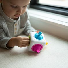 a young child playing with a toy in front of a window sill on the floor