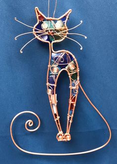 a cat made out of wire and beads on a blue background with the tail curled up