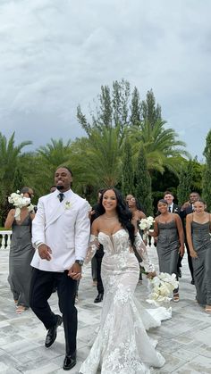 a bride and groom walking down the aisle with their bridal party in the background