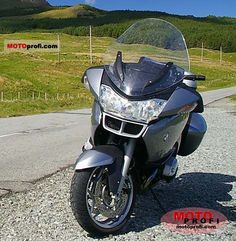 the motorcycle is parked on the side of the road in front of some hills and grass