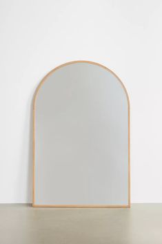 an arched mirror sitting on top of a table next to a white wall with a wooden frame