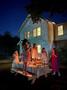 children are gathered around a table with food on it in front of a house at night