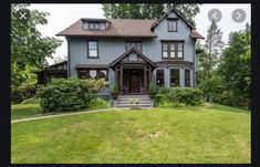 a large blue house sitting in the middle of a lush green field with lots of trees