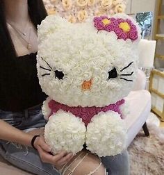 a woman sitting on a couch holding a hello kitty stuffed animal with roses all over it