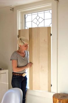 a woman standing in front of a window holding a piece of wood up against the wall