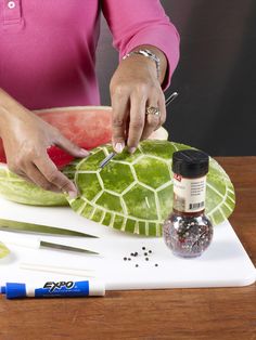 a woman cutting up a piece of watermelon on top of a wooden table