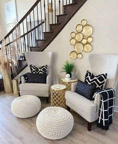 a living room with white chairs and black and gold pillows on the floor next to a stair case