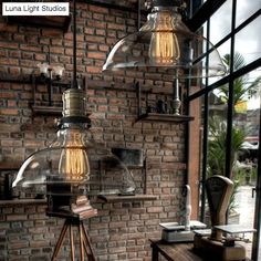 an industrial style lamp hanging from a brick wall next to a wooden table and chair