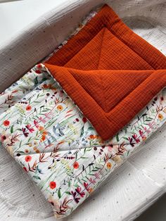 an orange piece of cloth sitting on top of a white tray next to a pillow