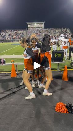 the cheerleaders huddle together in front of an orange cone at a football game