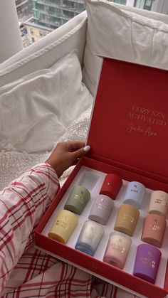 a person sitting on a couch holding an open box with nine different colored cups in it