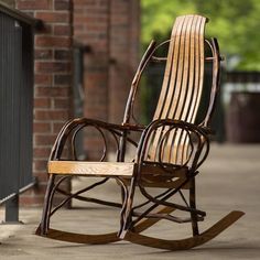 a wooden rocking chair sitting on top of a sidewalk next to a brick wall and fence