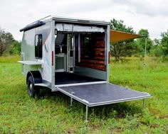 an enclosed trailer is parked in the middle of a grassy field with trees and grass