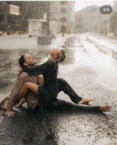 a man and woman sitting on the ground in the rain with their arms around each other