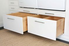 two drawers are open on the floor in front of white cupboards with handles and pulls