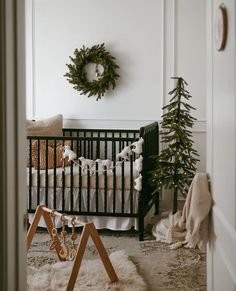 a baby's crib with a christmas wreath on the wall and a tree in the corner