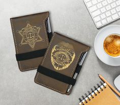 two brown leather notebooks sitting on top of a desk next to a cup of coffee