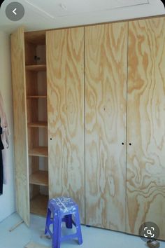 an unfinished closet with wooden walls and blue stools in the foreground, next to a white wall