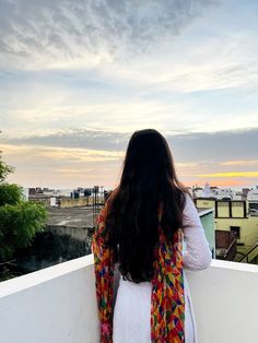 a woman standing on top of a roof next to a white wall and looking out at the city