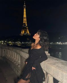 a woman in black dress standing next to the eiffel tower