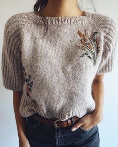 a woman is wearing a sweater with flowers on the front and back, while she has her hands in her pockets