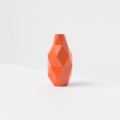 an orange geometric vase sitting on top of a white table next to a gray wall