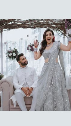 a man and woman sitting on a couch in front of a wedding arch with flowers