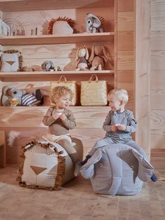 two young children sitting on top of stuffed animals in a room with wooden walls and shelves