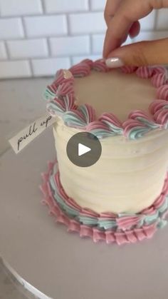 someone is decorating a cake with pink and blue icing on the bottom layer