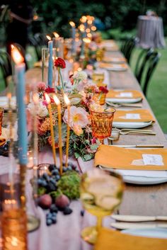 a long table is set with candles and plates for an elegant dinner party in the garden