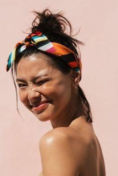 a woman wearing a colorful headband smiles at the camera while standing in front of a pink wall