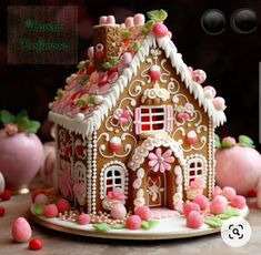 a gingerbread house decorated with pink and white icing on a table next to candy