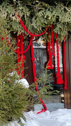 a red ribbon tied to the side of a building with evergreens and other greenery