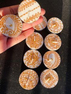 a person is holding several small white and gold decorated buttons in their left hand, on a black surface