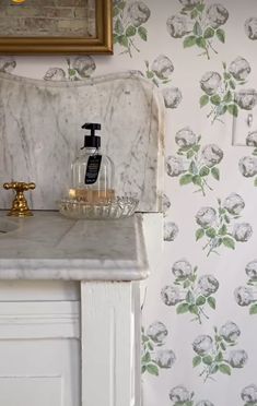 a marble sink with soap and lotion in front of a floral wallpapered bathroom