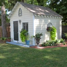 a small white shed with potted plants on the side