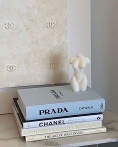 a stack of books sitting on top of a table next to a white vase filled with flowers