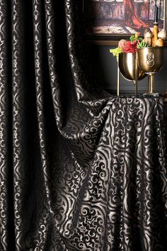 a gold vase sitting on top of a table next to a black and white curtain