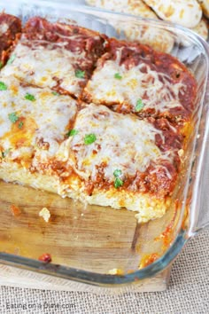 lasagna casserole in a glass dish on a wooden cutting board next to crackers