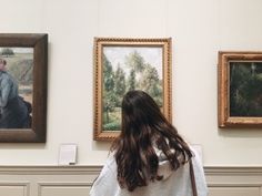 a woman looking at paintings on display in a museum